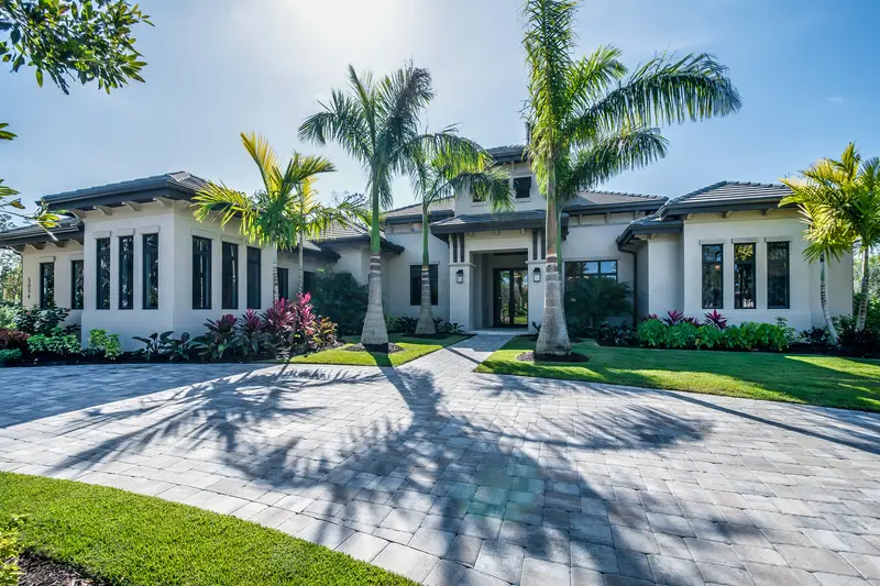 Luxury estate home featuring palm trees and a spacious paved stone driveway.
