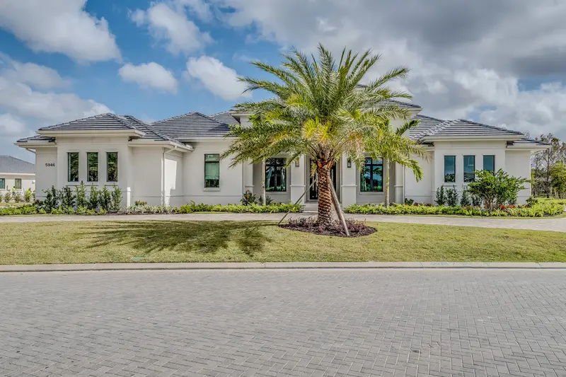 Modern luxury stucco villa with a manicured front lawn and central palm tree.