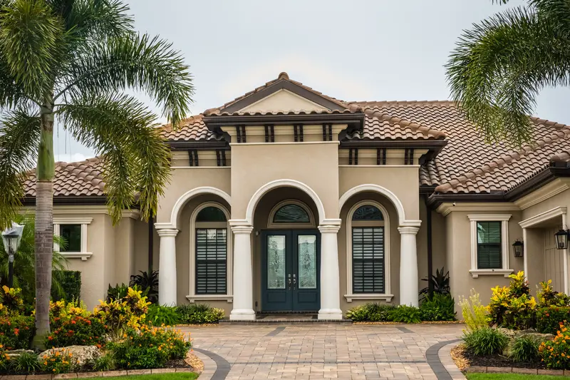 Luxury home with palm trees, paved driveway, and colorful landscaping
